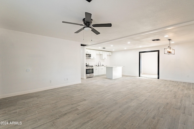 unfurnished living room with ceiling fan, light wood-type flooring, and sink