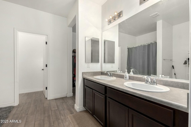 full bathroom featuring double vanity, wood finished floors, a sink, and a walk in closet