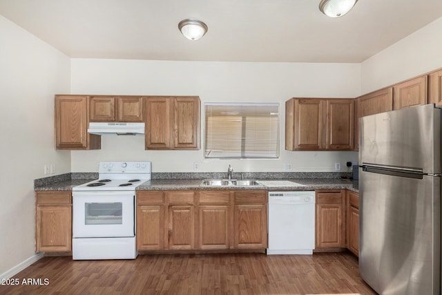 kitchen with a sink, under cabinet range hood, dark countertops, wood finished floors, and white appliances