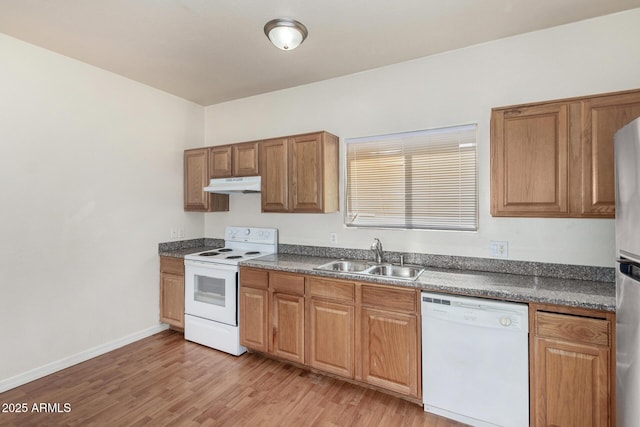 kitchen featuring light wood-style flooring, under cabinet range hood, a sink, dark countertops, and white appliances