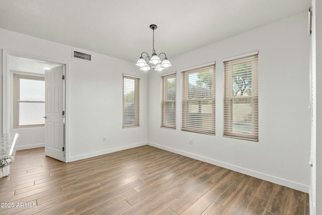 spare room with plenty of natural light, dark wood-type flooring, and an inviting chandelier