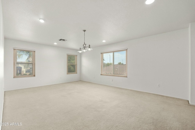 carpeted spare room featuring an inviting chandelier