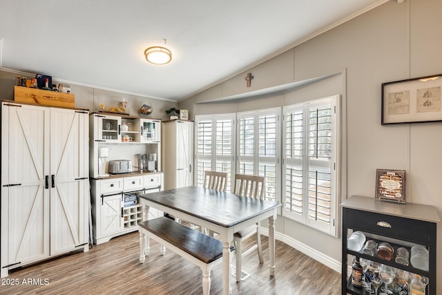 dining room featuring a toaster, crown molding, light wood-style flooring, vaulted ceiling, and baseboards