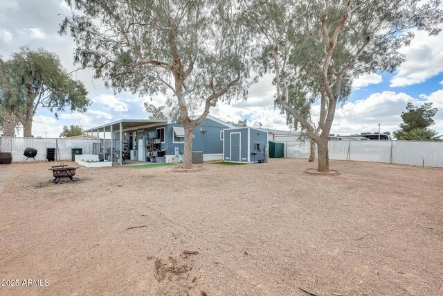 back of house with an outdoor fire pit, a storage unit, a fenced backyard, and an outbuilding