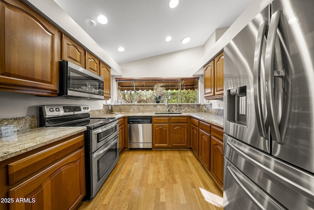 kitchen featuring appliances with stainless steel finishes, vaulted ceiling, sink, light wood-type flooring, and light stone counters