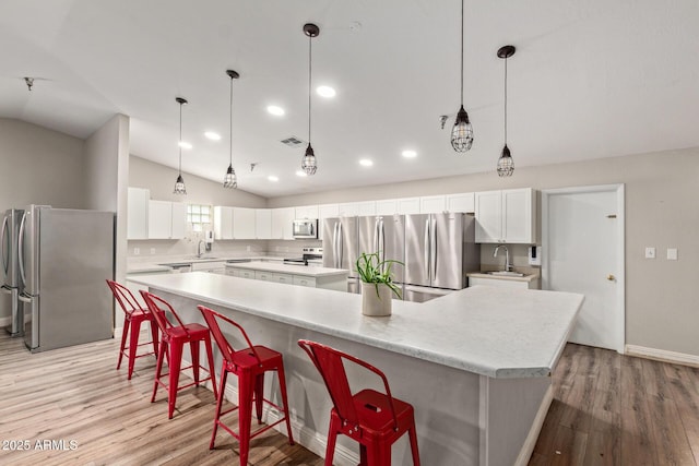 kitchen with stainless steel appliances, a large island, a sink, lofted ceiling, and light wood-style floors