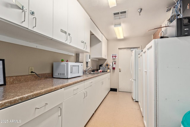 kitchen featuring white appliances, white cabinetry, and a sink