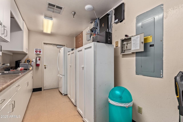 kitchen featuring electric panel, a sink, white cabinets, freestanding refrigerator, and light flooring