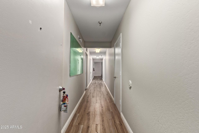 hallway featuring wood finished floors, baseboards, and attic access