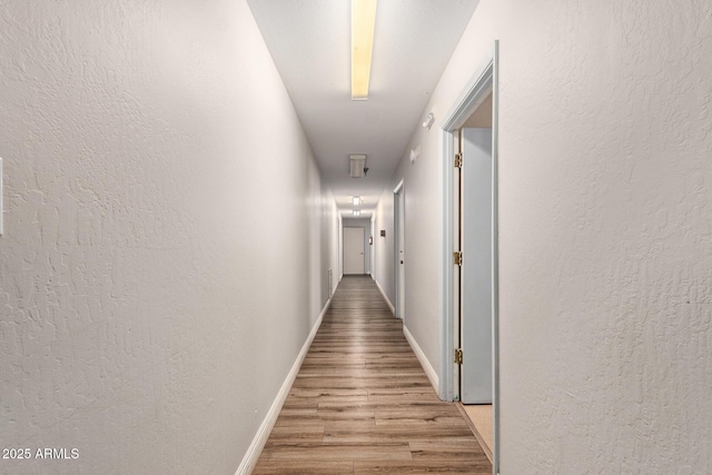 corridor featuring light wood-style flooring, baseboards, and a textured wall