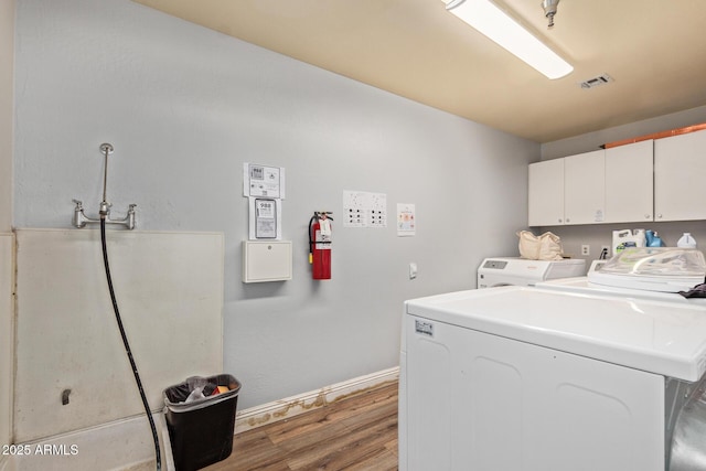 laundry room featuring cabinet space, wood finished floors, washing machine and dryer, and baseboards