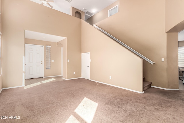 unfurnished living room with ceiling fan, a towering ceiling, and light colored carpet