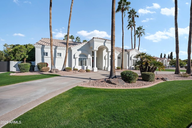 view of front of house with driveway, a tiled roof, fence, a front lawn, and stucco siding