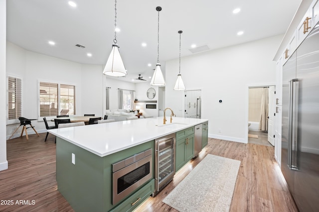 kitchen featuring beverage cooler, visible vents, green cabinetry, built in appliances, and a sink