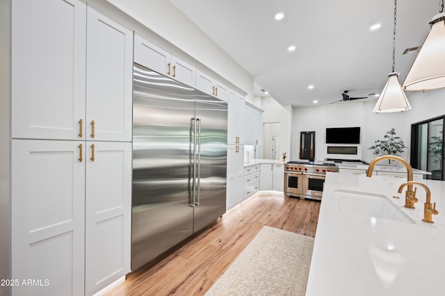 kitchen featuring premium appliances, recessed lighting, light countertops, a sink, and light wood-type flooring