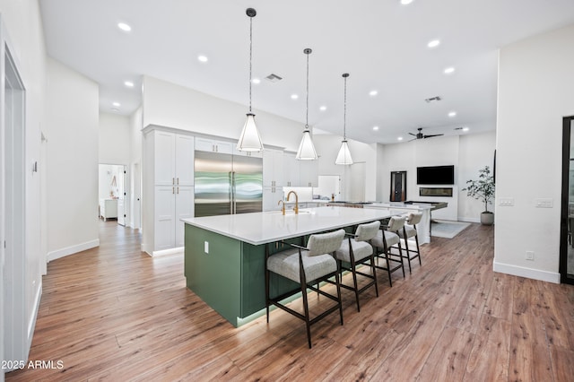 kitchen featuring light wood-type flooring, light countertops, a large island with sink, and built in fridge