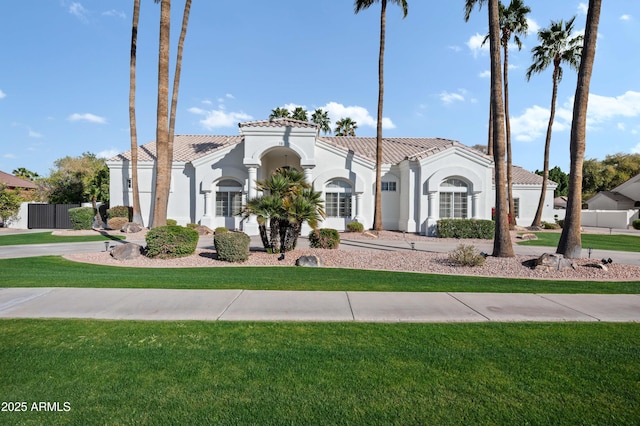 mediterranean / spanish-style house with fence, a tiled roof, a front lawn, and stucco siding