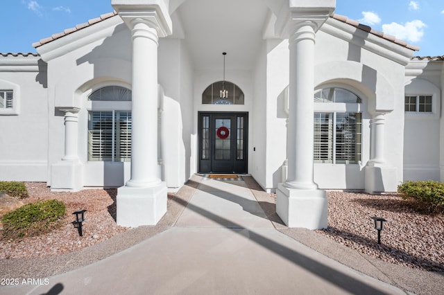 view of exterior entry with a tiled roof and stucco siding