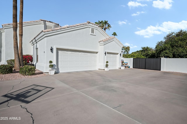 view of side of home with an attached garage, fence, driveway, a tiled roof, and stucco siding