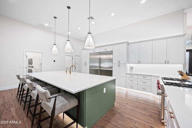 kitchen with premium appliances, light countertops, light wood-style floors, a kitchen island with sink, and a kitchen breakfast bar