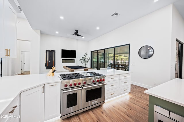 kitchen with range with two ovens, light countertops, white cabinets, and visible vents