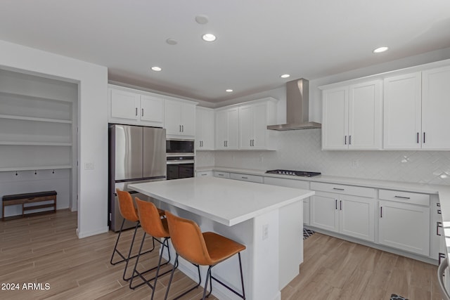 kitchen featuring wall chimney exhaust hood, stainless steel appliances, light hardwood / wood-style flooring, white cabinets, and a kitchen island