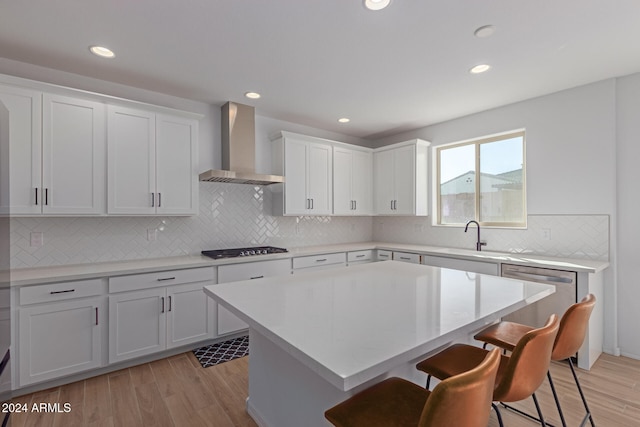 kitchen with appliances with stainless steel finishes, wall chimney exhaust hood, light hardwood / wood-style flooring, white cabinets, and a kitchen island