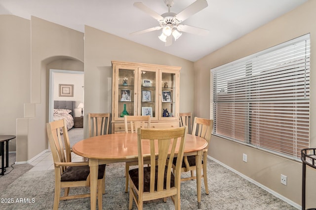 dining room with vaulted ceiling, light tile patterned floors, baseboards, arched walkways, and ceiling fan