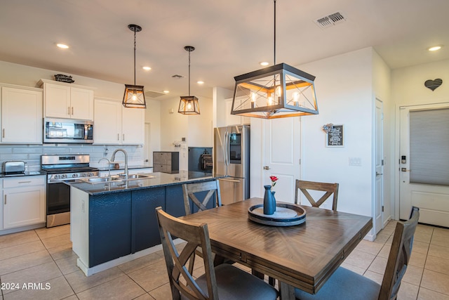 kitchen with stainless steel appliances, a center island with sink, dark stone countertops, white cabinets, and hanging light fixtures