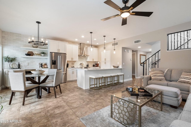 living area featuring ceiling fan with notable chandelier, visible vents, baseboards, and stairs