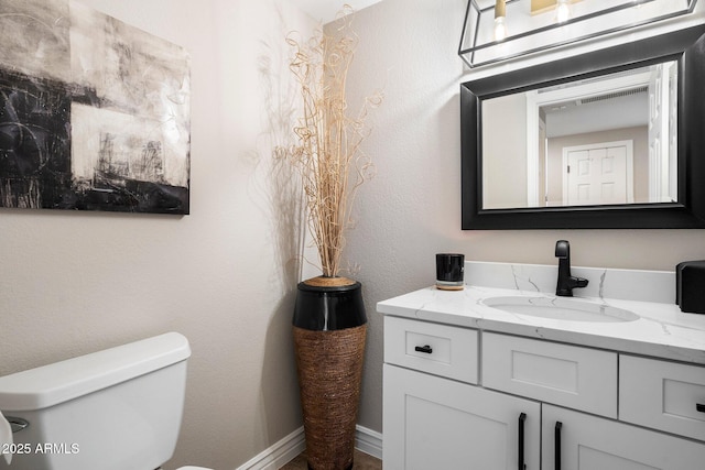 half bath featuring a textured wall, vanity, and toilet