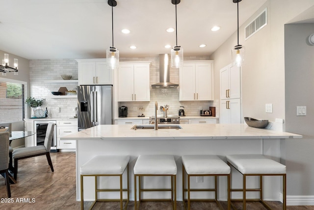 kitchen with high end fridge, visible vents, white cabinets, a sink, and wall chimney exhaust hood