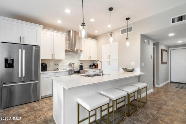 kitchen with wall chimney range hood, visible vents, appliances with stainless steel finishes, and a sink