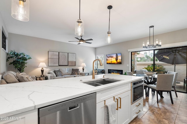 kitchen with stainless steel appliances, a sink, white cabinets, open floor plan, and a glass covered fireplace