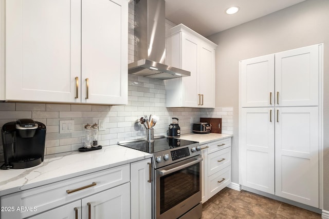 kitchen with light stone counters, backsplash, white cabinets, wall chimney range hood, and stainless steel electric range