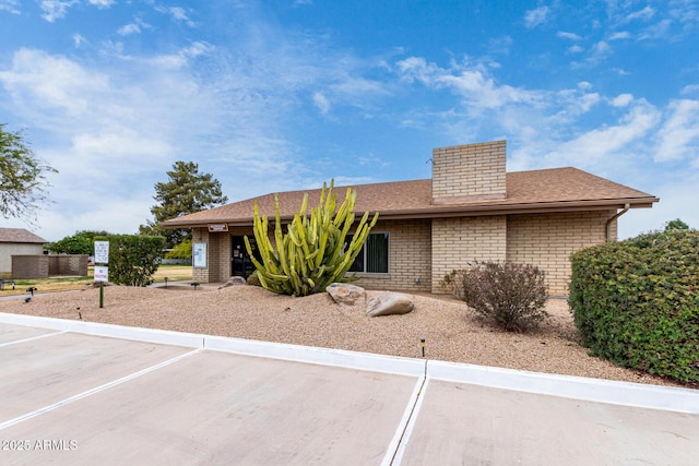 ranch-style home featuring uncovered parking, a chimney, brick siding, and roof with shingles