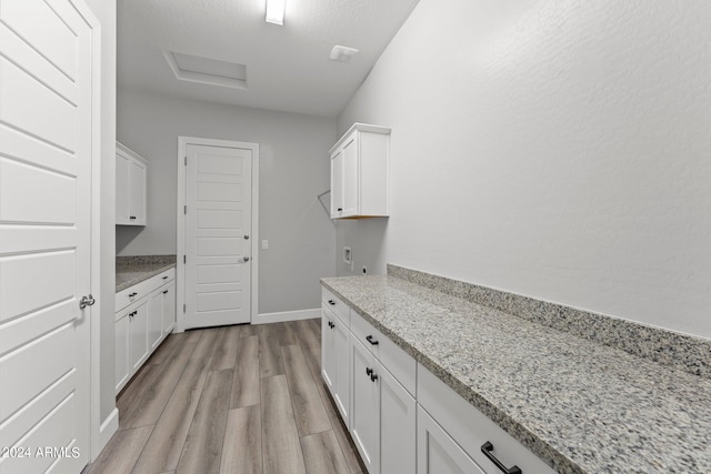 kitchen featuring white cabinetry, light stone counters, a textured ceiling, and light wood-type flooring