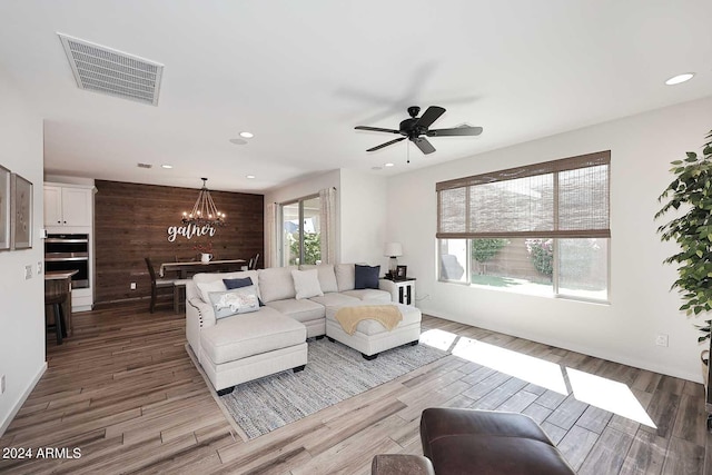 living room with ceiling fan with notable chandelier, wood walls, wood-type flooring, and a healthy amount of sunlight