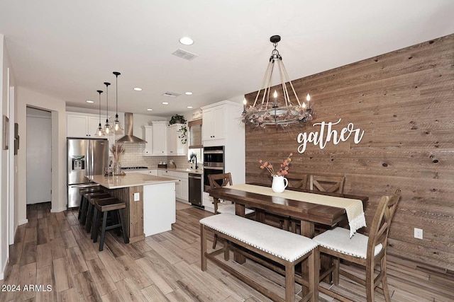 dining space with wooden walls, light hardwood / wood-style flooring, a chandelier, and sink