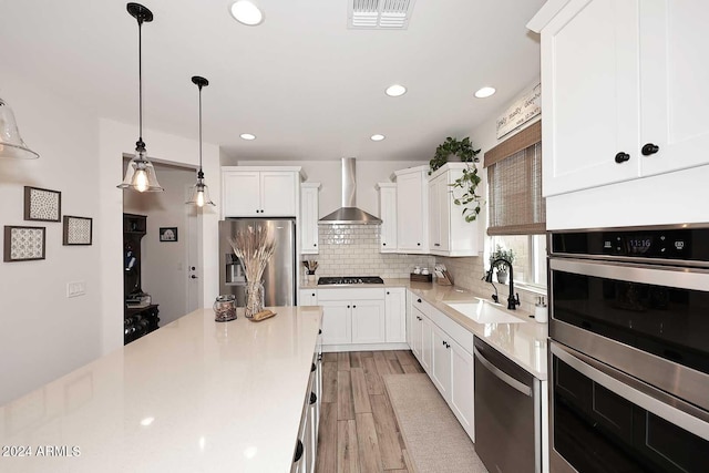 kitchen with white cabinets, wall chimney range hood, sink, and appliances with stainless steel finishes