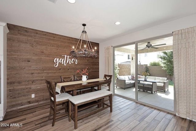 dining room with hardwood / wood-style flooring, ceiling fan with notable chandelier, and wood walls