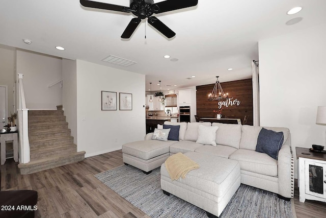 living room featuring wood-type flooring, ceiling fan with notable chandelier, wooden walls, and sink