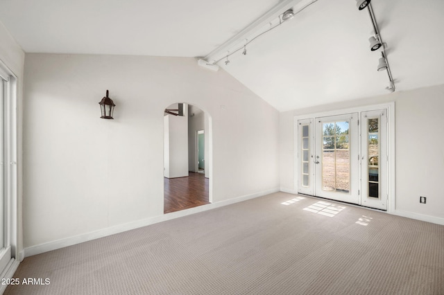 unfurnished room featuring arched walkways, baseboards, vaulted ceiling, and carpet