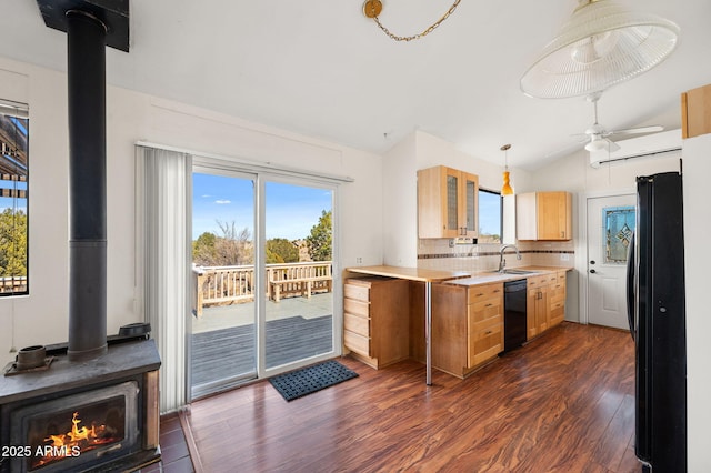 kitchen featuring light countertops, light brown cabinets, a sink, black appliances, and a wood stove