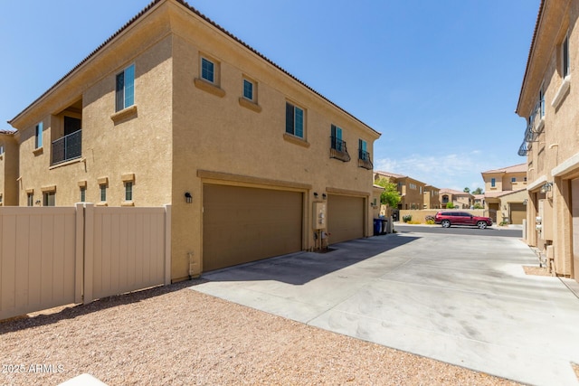 view of property exterior featuring a residential view, a garage, stucco siding, fence, and driveway