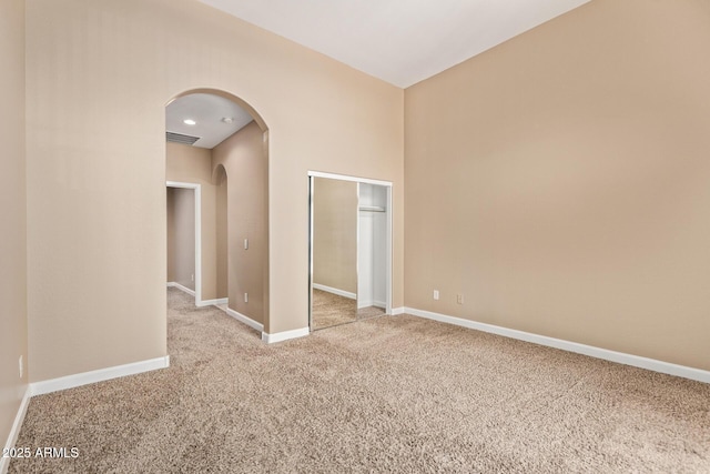 empty room featuring carpet flooring, arched walkways, baseboards, and visible vents