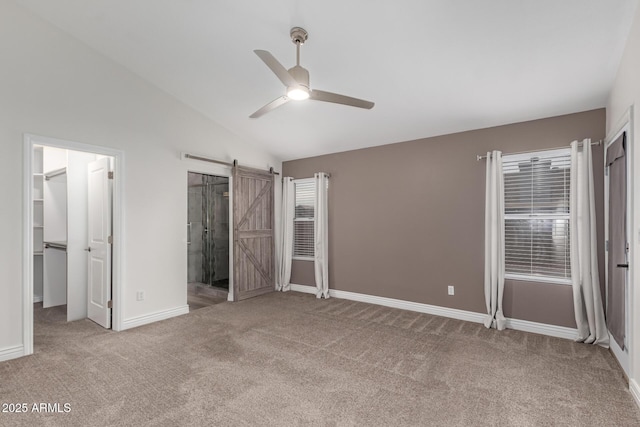 unfurnished bedroom featuring baseboards, lofted ceiling, a walk in closet, a barn door, and carpet flooring