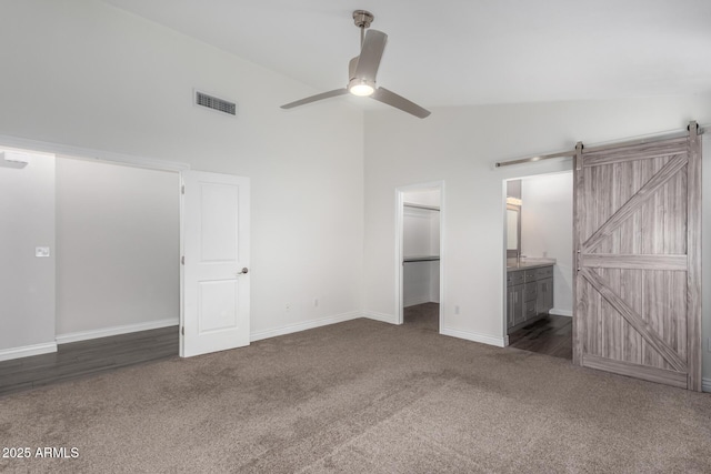 unfurnished bedroom featuring a spacious closet, visible vents, carpet, a barn door, and ensuite bathroom