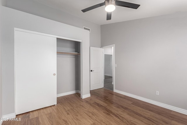 unfurnished bedroom with visible vents, lofted ceiling, wood finished floors, a closet, and baseboards