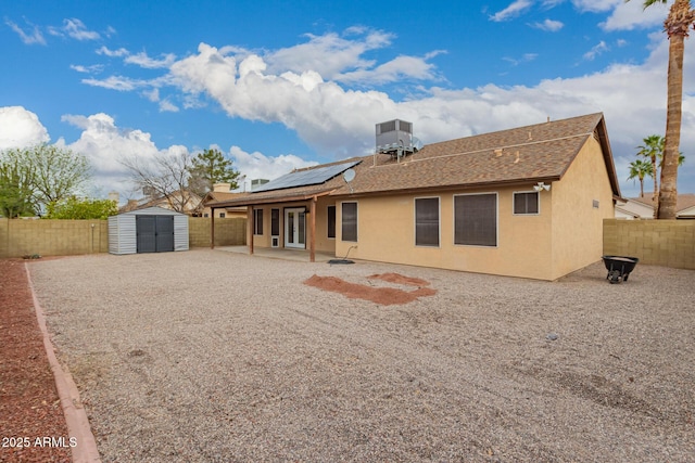 rear view of property featuring stucco siding, french doors, a storage unit, and a fenced backyard